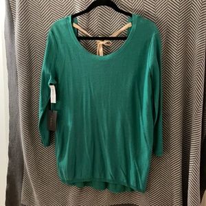 Green open back sweater with nude colored tie across shoulders.